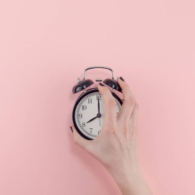 Yaratıcı düz sabah zaman duygular kadın el Siyah vintage çalar saat pastel bin yıllık pembe renkli kağıt arka plan kopya alanı en az tarzı kare şablonuyla tutarak en iyi görünümünü kavramı yatıyordu.