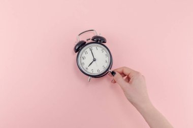 Yaratıcı düz sabah zaman duygular kavramı en iyi siyah vintage çalar saat pastel bin yıllık pembe renkli kağıt arka plan metin için kopya alanı en az stil şablonu ile birlikte tutan kadın el görünümünü yatıyordu.