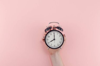 Yaratıcı düz sabah zaman duygular kavramı en iyi siyah vintage çalar saat pastel bin yıllık pembe renkli kağıt arka plan metin için kopya alanı en az stil şablonu ile birlikte tutan kadın el görünümünü yatıyordu.