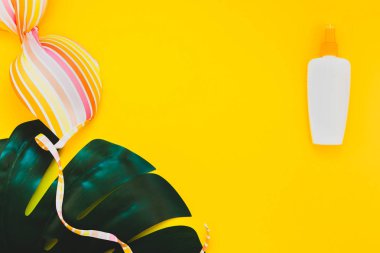 Tropikal orman palm monstera bırakır, güneş gözlüğü, güneş kremi boş şişe mockup ve kadının mayo üst parlak sarı kağıt arka plan üzerinde. Metin için yaratıcı düz yatıyordu kavramı şablon yaz tatil