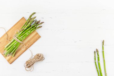 Beyaz ahşap arka planda taze yeşil kuşkonmaz.