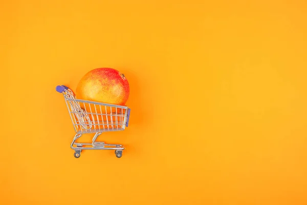 주황색 배경에 쇼핑 카트에 망고 과일 — 스톡 사진