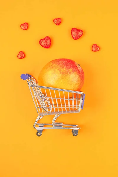 주황색 배경에 쇼핑 카트에 망고 과일 — 스톡 사진