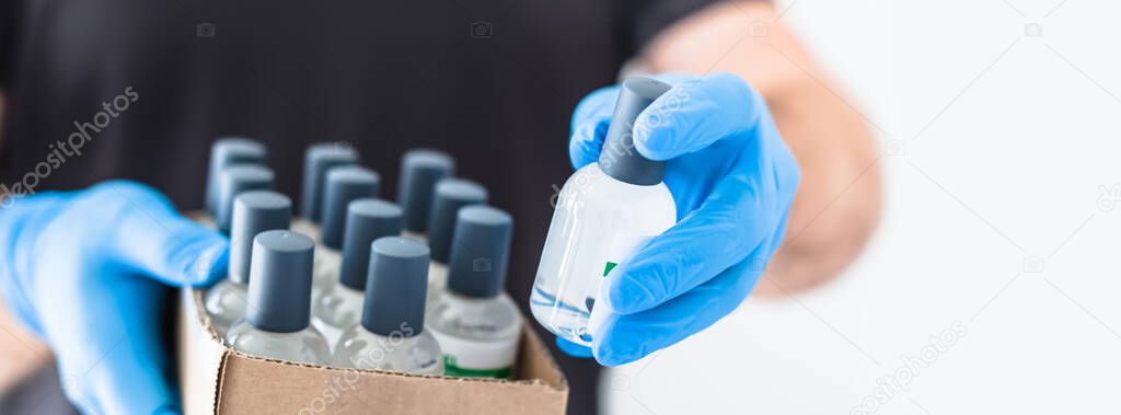 Hand sanitizer hygiene alcohol gel bottles in hands of man wearing latex medical gloves and protective mask during coronavirus COVID-19 pandemics. Healthcare hygiene and safety measures