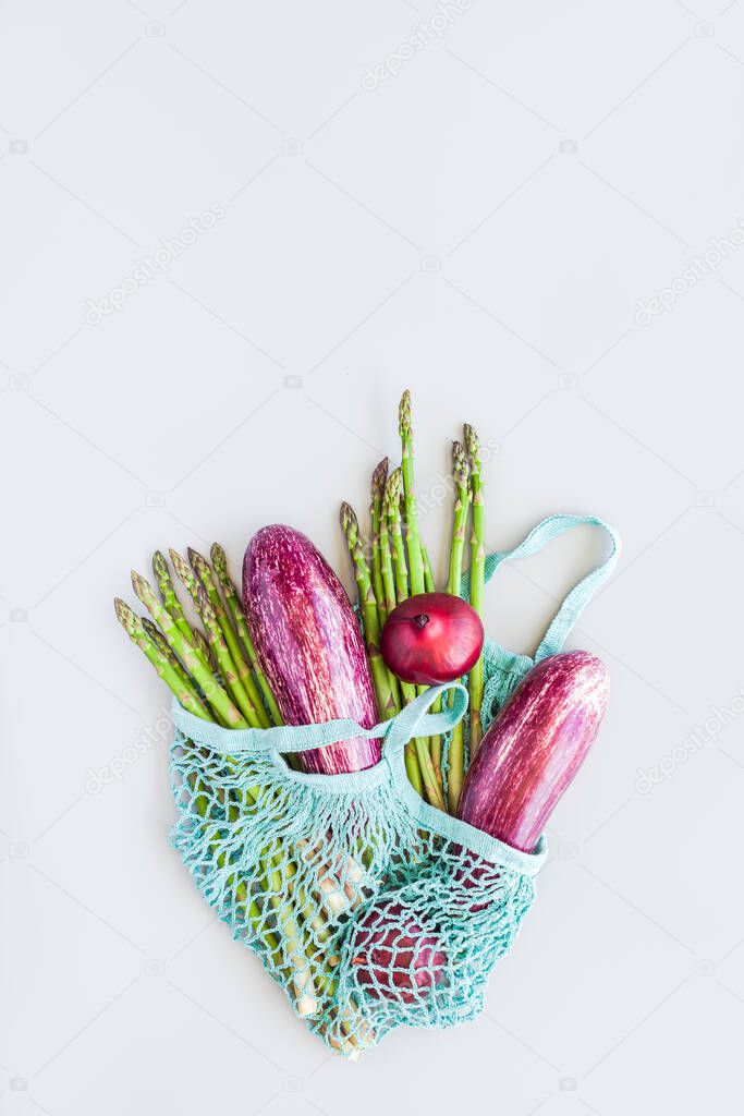 Fresh organic vegetables in blue eco reusable cotton mesh shopping bag flat lay, top view with copy space on gray background. Sustainable lifestyle. Zero waste, plastic free concept.