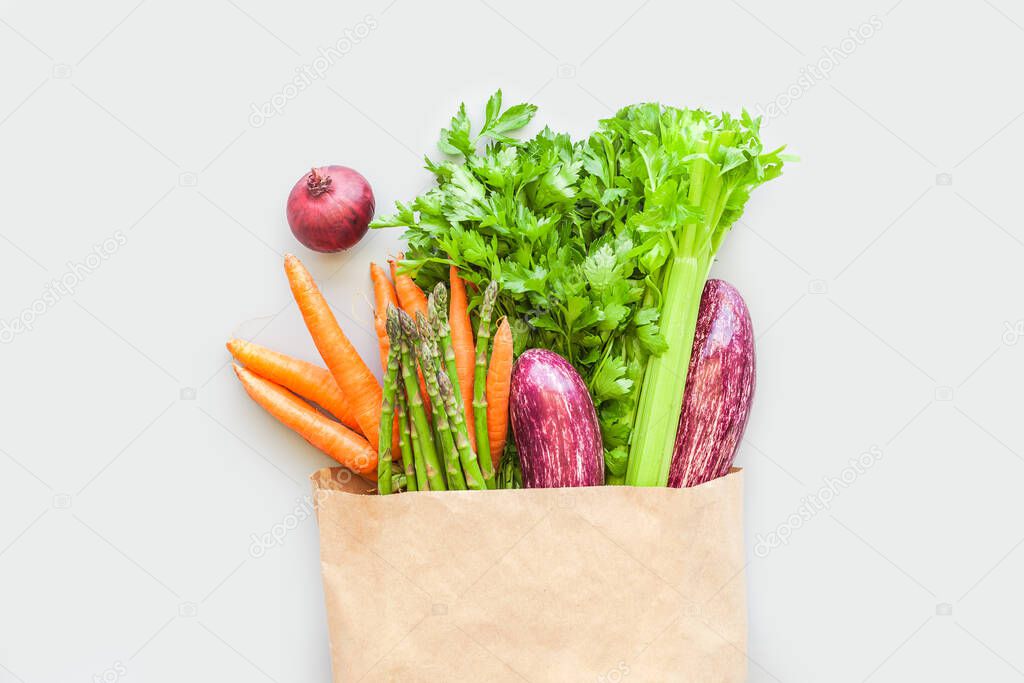 Fresh organic vegetables in eco craft paper shopping bag  in flat lay, top view with copy space on gray background. Sustainable lifestyle. Zero waste, plastic free, care package, donation concept