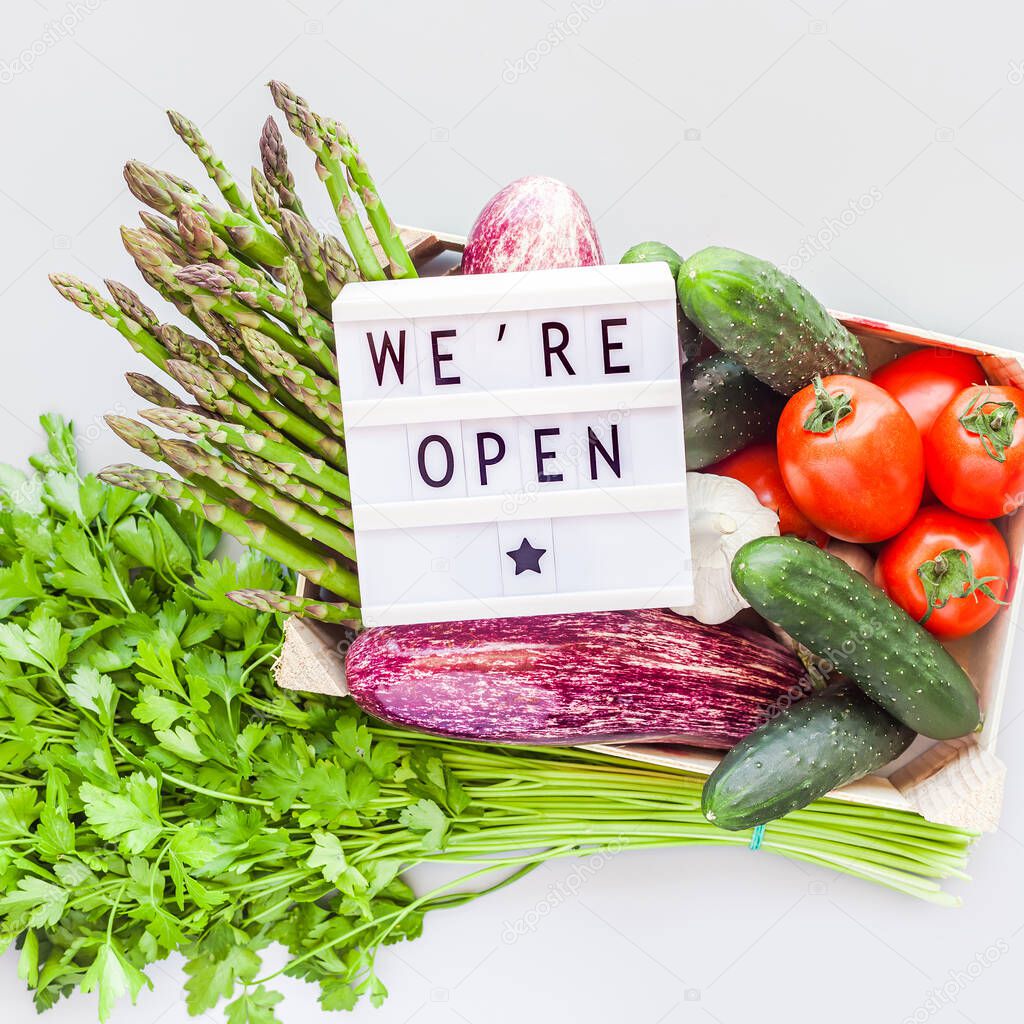 End of quarantine. Fresh organic vegetables in eco friendly wooden box with text We're Open lightbox flat lay, top view on gray background. Sustainable lifestyle. Zero waste, plastic free concept