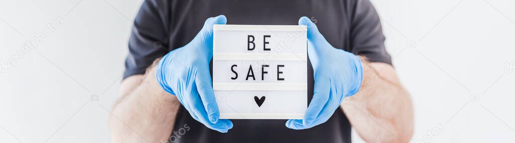 Healthcare and Safety concept. Man wearing latex medical gloves on his hands and protective mask holding lightbox with text Be safe during coronavirus COVID-19 pandemics