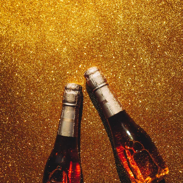 Christmas or New Year composition with bottles of rose champagne on golden shiny background, top view with dark shadows. Celebration flat lay. Party creative concept