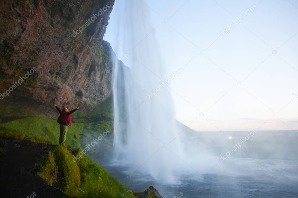 Woman tourist near the Seljalandsfoss waterfall during the sunset, Iceland