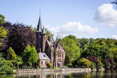 Minnewater gölü panoraması, gotik yapının yansıması ve Castle de la Faille yakınlarındaki kafede insanlar, bulutlu mavi gökyüzü, Bruges, Belçika