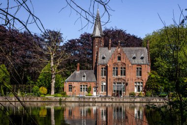 Minnewater gölü panoraması, gotik yapının yansıması ve Castle de la Faille yakınlarındaki kafede insanlar, bulutlu mavi gökyüzü, Bruges, Belçika