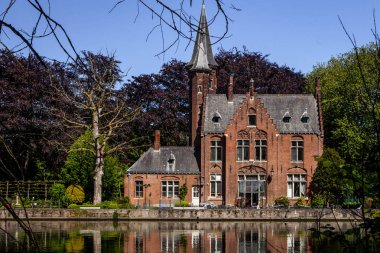 Minnewater gölü panoraması, gotik yapının yansıması ve Castle de la Faille yakınlarındaki kafede insanlar, bulutlu mavi gökyüzü, Bruges, Belçika