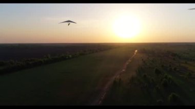 Askılı planör uçuşu günbatımında yeşil ve sarı taze bahar tarlaları üzerinde. Havadan görünüşlü. İnsansız hava aracı ile çekildi.