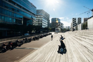 Paris, Fransa - 5 Ekim 2016: Paris 'teki Fransız Ulusal Kütüphanesi kuleleri ve güneşli bir günde plazaya çıkan merdivenler, ahşap merdivenlerde kitap okuyan insanlar