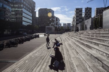 Paris, Fransa - 5 Ekim 2016: Paris 'teki Fransız Ulusal Kütüphanesi kuleleri ve güneşli bir günde plazaya çıkan merdivenler, ahşap merdivenlerde kitap okuyan insanlar