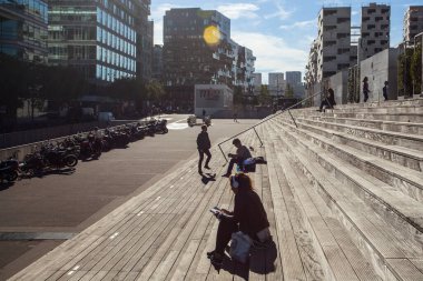 Paris, Fransa - 5 Ekim 2016: Paris 'teki Fransız Ulusal Kütüphanesi kuleleri ve güneşli bir günde plazaya çıkan merdivenler, ahşap merdivenlerde kitap okuyan insanlar
