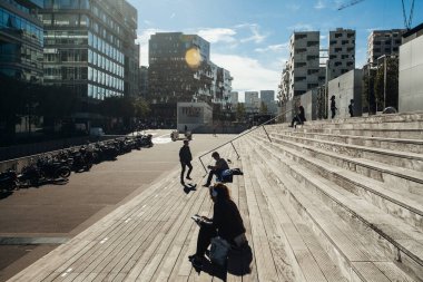 Paris, Fransa - 5 Ekim 2016: Paris 'teki Fransız Ulusal Kütüphanesi kuleleri ve güneşli bir günde plazaya çıkan merdivenler, ahşap merdivenlerde kitap okuyan insanlar