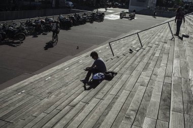 Paris, Fransa - 5 Ekim 2016: Paris 'teki Fransız Ulusal Kütüphanesi kuleleri ve güneşli bir günde plazaya çıkan merdivenler, ahşap merdivenlerde kitap okuyan insanlar