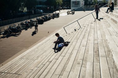 Paris, Fransa - 5 Ekim 2016: Paris 'teki Fransız Ulusal Kütüphanesi kuleleri ve güneşli bir günde plazaya çıkan merdivenler, ahşap merdivenlerde kitap okuyan insanlar