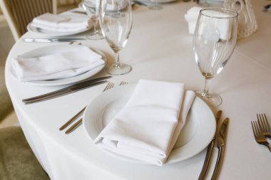 Yuvarlak masa beyaz masa örtüsü, tabaklar, gözlük ve çatal bıçak takımı ile kaplıdır