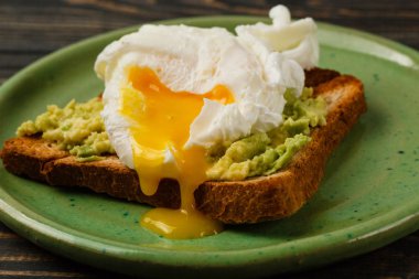 Kepekli ekmek tost ve ahşap masa üzerinde yeşil plaka üzerinde avokado ile haşlanmış yumurta