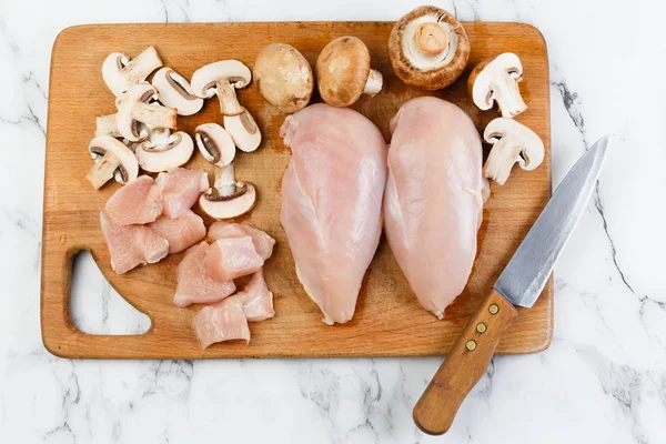 raw chicken fillets and mushrooms on a wooden board