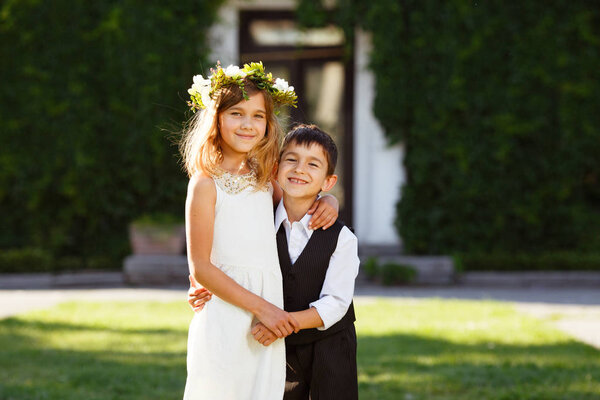 A girl in a white dress hugs a boy in a fashionable suit. Park, sunset