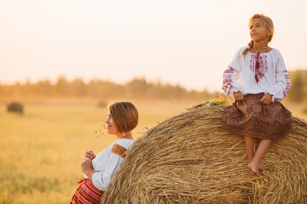 A girl and woman in embroidered clothes in the field in the background of the setting sun. Concept of countryside lifestyle, national traditions, ukrenian family.