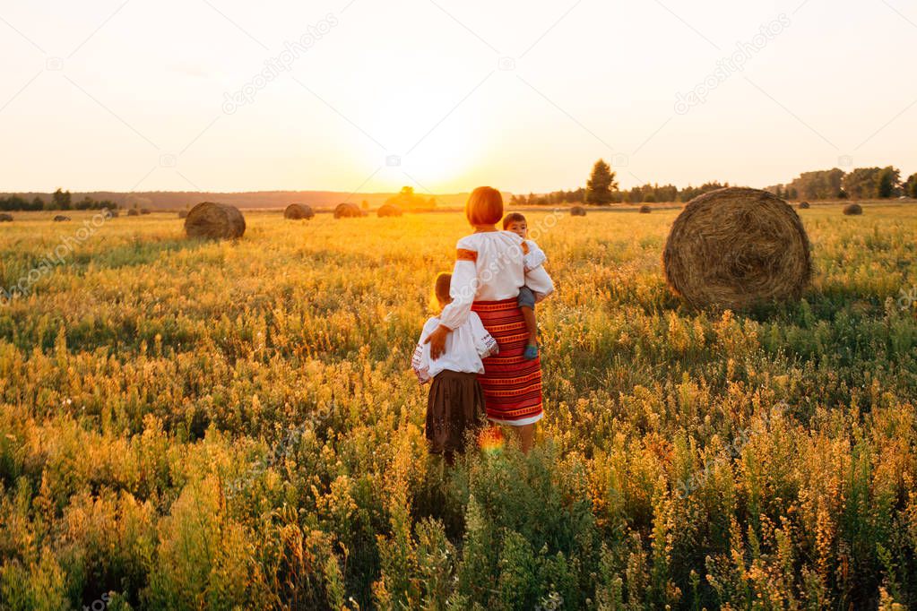 Family: my mother and son and daughter are walking along the field. They are dressed in embroidered robes. Sunset.