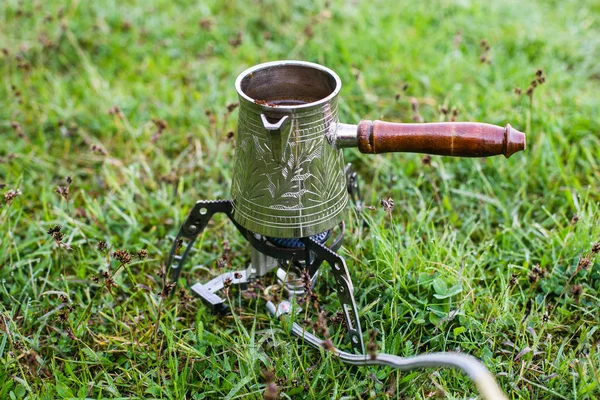 Small camping gas stove and small coffee cezve in the morning on grass