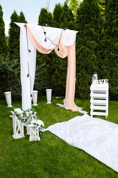 Wedding arch decorated with cloth outdoors. Beautiful wedding set up. Wedding ceremony on green lawn in the garden. Part of the festive decor.