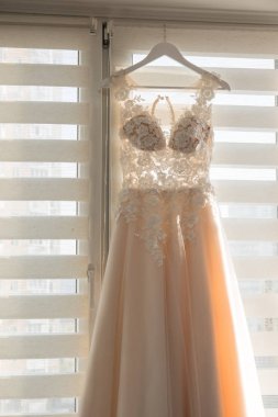 Bir askı bir pencere yakınında asılı parlak bej renkli gelinlik