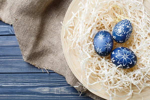 Hand painted dark blue easter eggs in nest and flowers on wooden — Stock Photo, Image