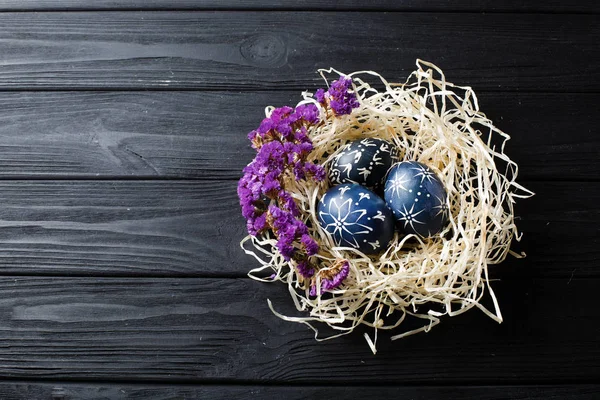 Hand painted dark blue easter eggs in nest and flowers on wooden table — Stock Photo, Image