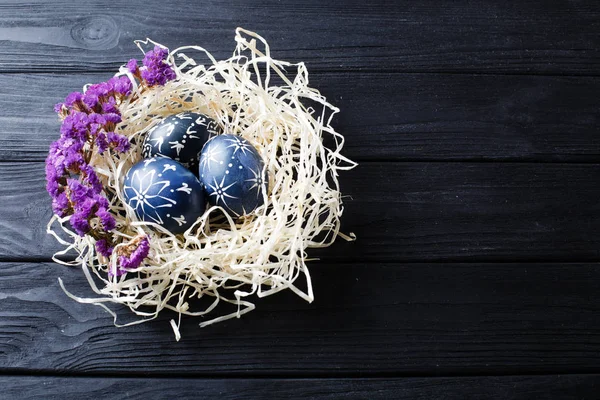 Hand painted dark blue easter eggs in nest and flowers on wooden — Stock Photo, Image