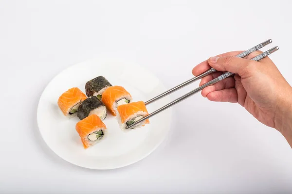 皿の上の寿司のロール タブレット上の寿司ロール 白い背景 寿司ロールと箸で手 — ストック写真