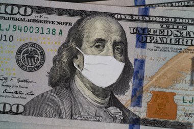 Coronovirus krizi konsepti. Üzerinde koruyucu maske olan ABD 'nin parası. Tahta masada yığınla para var. ABD 100 USD