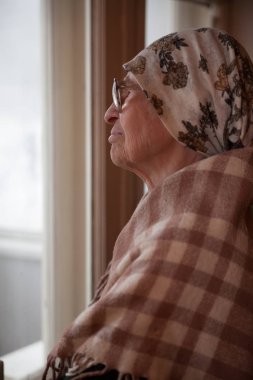   Yaşlı kadın eşarp ve gözlük evde pencere yakınındaki.