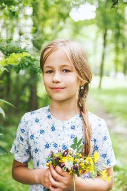 Parkta elinde çiçeklerle duran 8 yaşındaki kızın portresi.