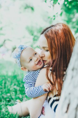    parkta kollarında anne tarafından oturan küçük kız.