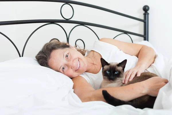 Beautiful older woman with   cat sleeping on   bed.