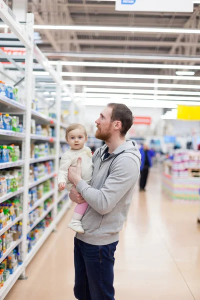 Father with   little daughter choosing  baby food on   shelves of   supermarket.