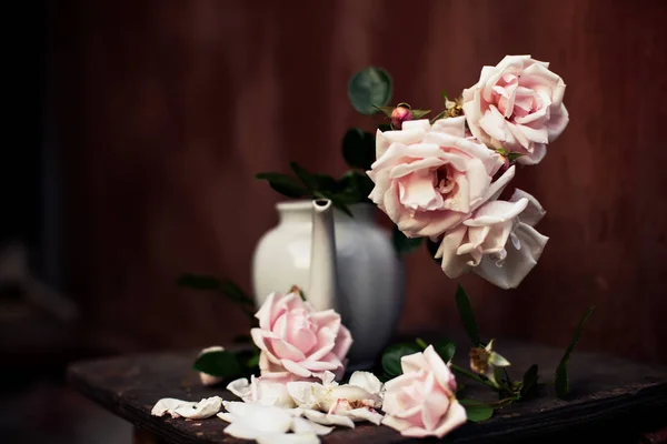 Beautiful still life of roses in   vase from   teapot on   brown background.