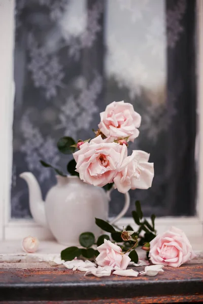 Beautiful still life of roses in   vase from   teapot on  windowsill.