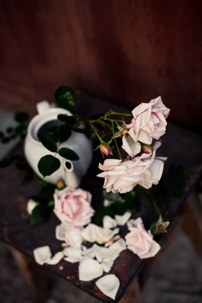 Beautiful still life of roses in   vase from   teapot on   brown background.