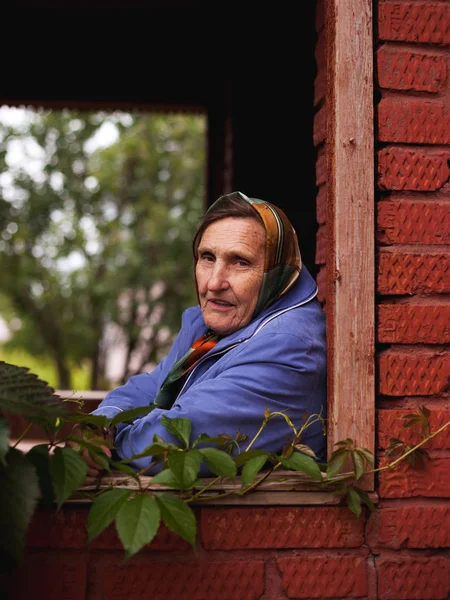 木造住宅のベランダに座るハンカチの老祖母 — ストック写真