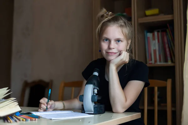 Schoolgirl studying chemistry with textbooks and   microscope.