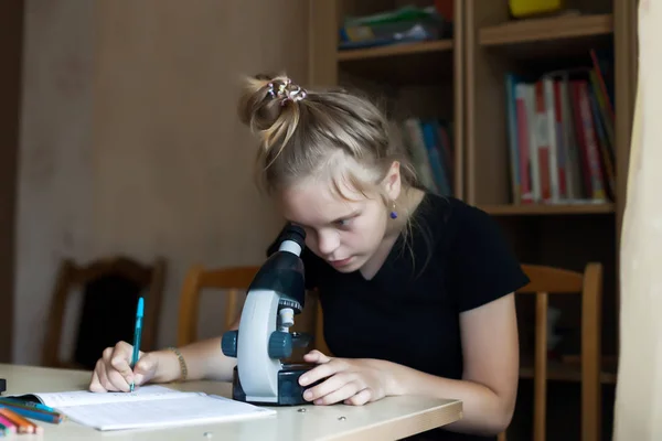 Schoolgirl studying chemistry with textbooks and   microscope.