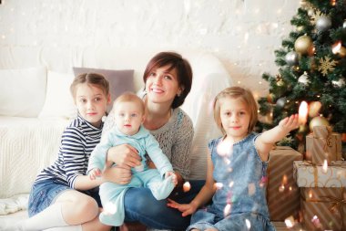 Üç kızı olan bir anne Noel ağacının yanında yerde oturuyor.